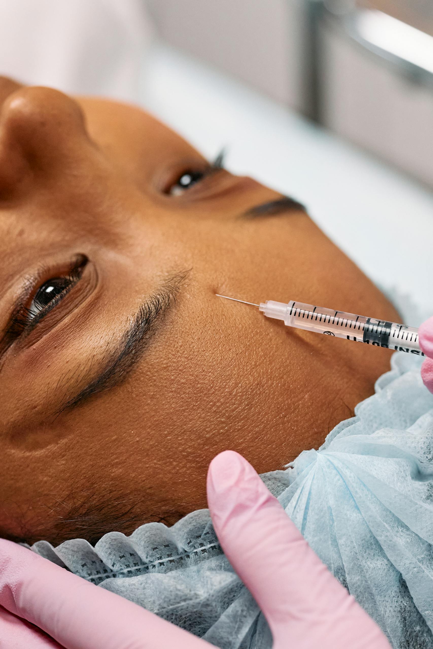 Close-up image of a cosmetic procedure showing a needle injecting into a forehead.